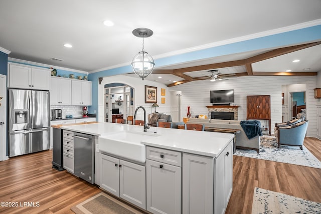 kitchen featuring a ceiling fan, a sink, a fireplace, a kitchen island with sink, and appliances with stainless steel finishes