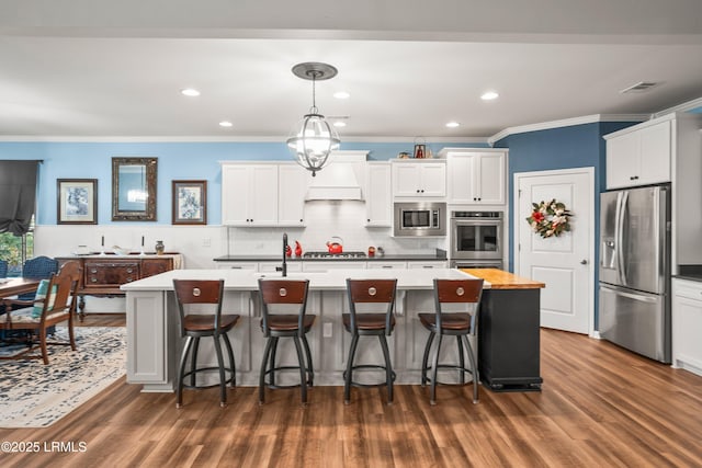 kitchen with tasteful backsplash, ornamental molding, an island with sink, white cabinets, and appliances with stainless steel finishes