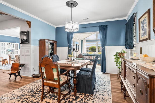 dining area featuring ornamental molding, wainscoting, a chandelier, a decorative wall, and wood finished floors