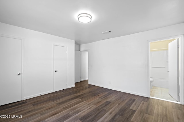 unfurnished bedroom featuring dark wood-type flooring, visible vents, baseboards, and ensuite bathroom