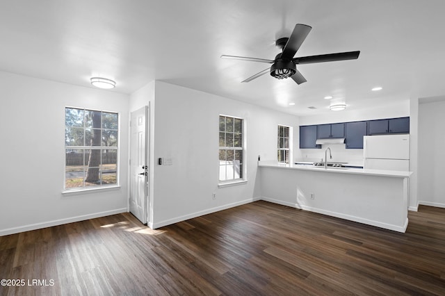 kitchen featuring under cabinet range hood, dark wood-style floors, freestanding refrigerator, a peninsula, and light countertops