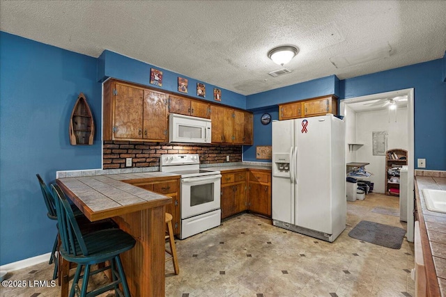 3003 Cherry Blvd, Beaufort, SC 29902 - kitchen with white appliances, tile countertops, brown cabinetry, a peninsula, and a textured ceiling