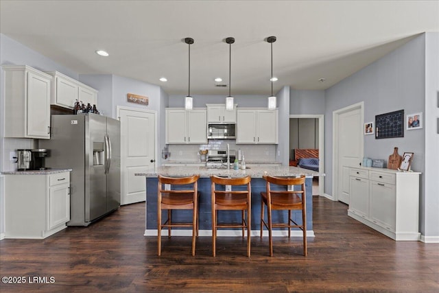 kitchen featuring white cabinetry, appliances with stainless steel finishes, decorative light fixtures, and an island with sink