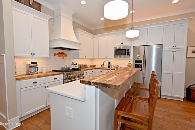 kitchen featuring premium appliances, tasteful backsplash, wood counters, wood finished floors, and premium range hood