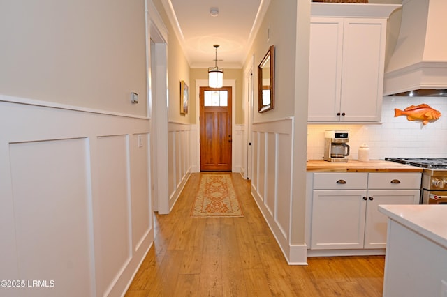 doorway to outside featuring a wainscoted wall, light wood finished floors, and ornamental molding