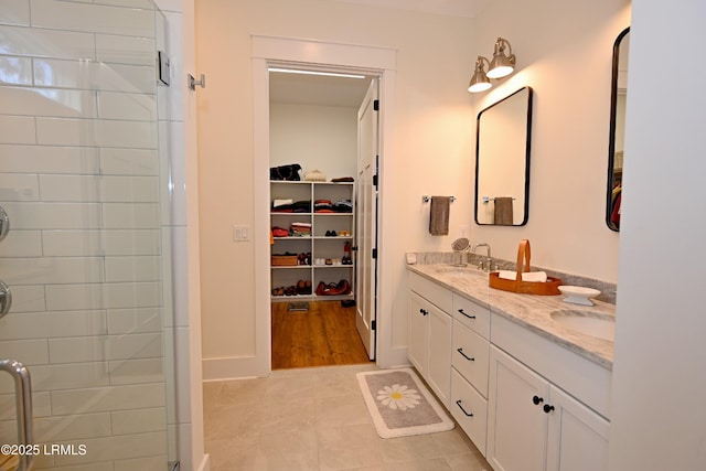 full bathroom featuring a spacious closet, double vanity, a sink, and a shower stall