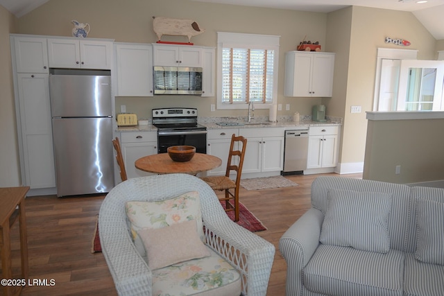 kitchen with stainless steel appliances, wood finished floors, a sink, white cabinetry, and vaulted ceiling