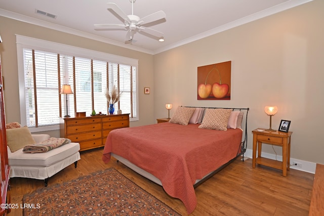 bedroom featuring baseboards, visible vents, crown molding, and wood finished floors