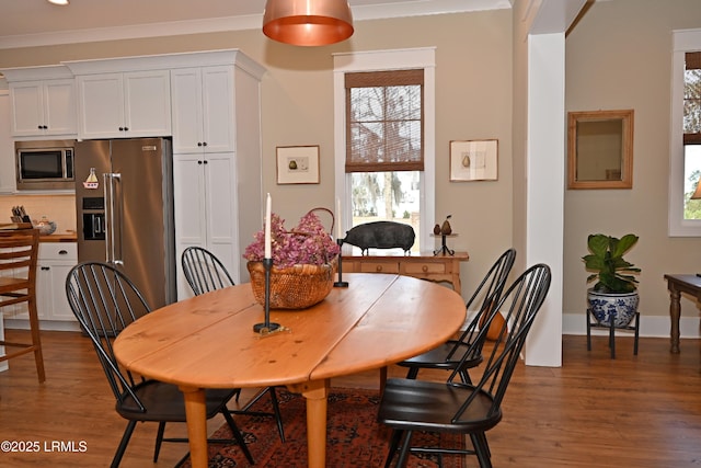 dining space featuring dark wood-type flooring, crown molding, and baseboards