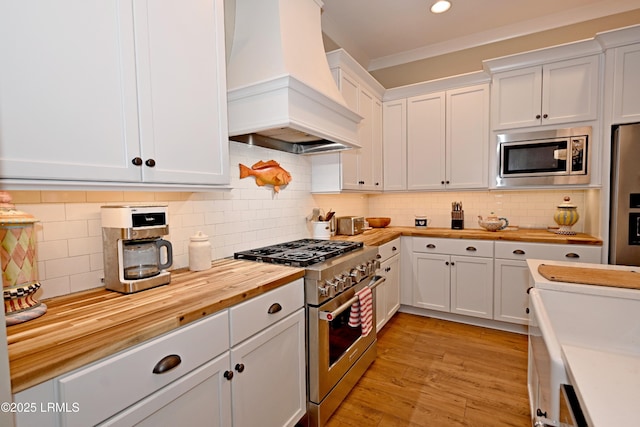 kitchen featuring white cabinets, wood counters, appliances with stainless steel finishes, ornamental molding, and premium range hood