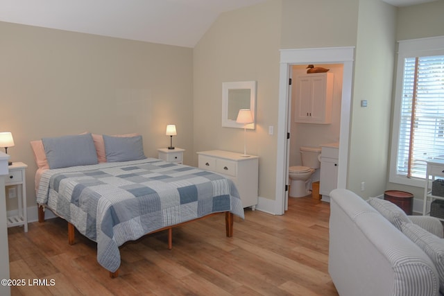 bedroom featuring light wood-style floors, connected bathroom, vaulted ceiling, and baseboards