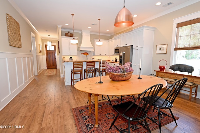 dining area featuring wainscoting, ornamental molding, light wood-type flooring, and visible vents