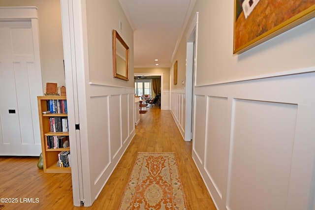 corridor with a wainscoted wall, light wood finished floors, and a decorative wall