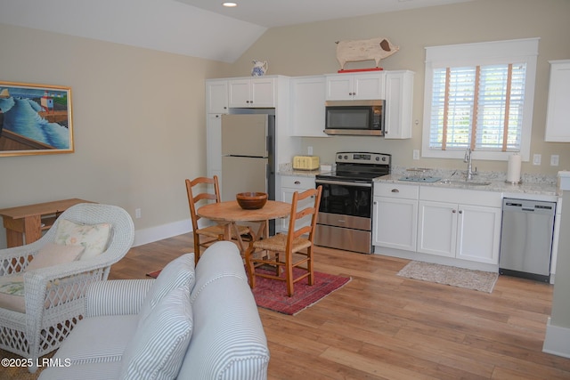 kitchen with lofted ceiling, a sink, white cabinets, appliances with stainless steel finishes, and light wood finished floors