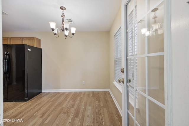 kitchen featuring black refrigerator, hanging light fixtures, a notable chandelier, light brown cabinets, and light hardwood / wood-style flooring