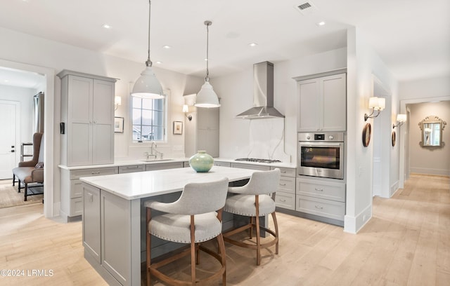 kitchen featuring wall chimney exhaust hood, sink, a center island, appliances with stainless steel finishes, and gray cabinets