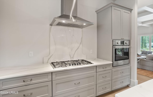 kitchen with gray cabinetry, light stone counters, ventilation hood, and stainless steel appliances