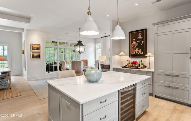 kitchen with beverage cooler, a center island, light wood-type flooring, and decorative light fixtures