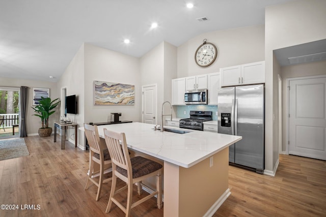 kitchen with appliances with stainless steel finishes, white cabinetry, an island with sink, a breakfast bar area, and light stone countertops