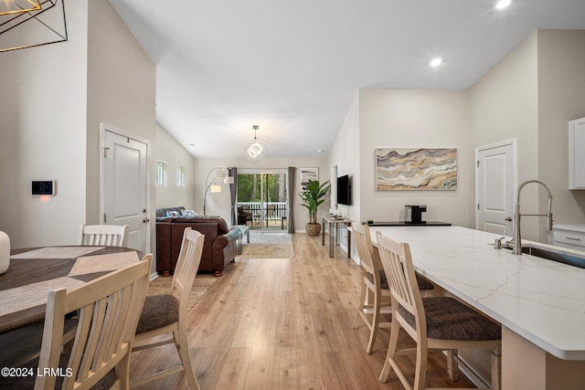 dining room with sink, light hardwood / wood-style floors, and high vaulted ceiling