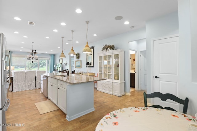 127 Kings Creek Dr, Bluffton, SC 29909 - kitchen featuring light wood finished floors, light stone countertops, a center island with sink, decorative light fixtures, and white cabinetry