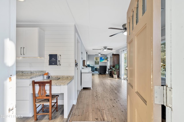 kitchen with white cabinetry, a kitchen breakfast bar, ceiling fan, light stone countertops, and light hardwood / wood-style floors