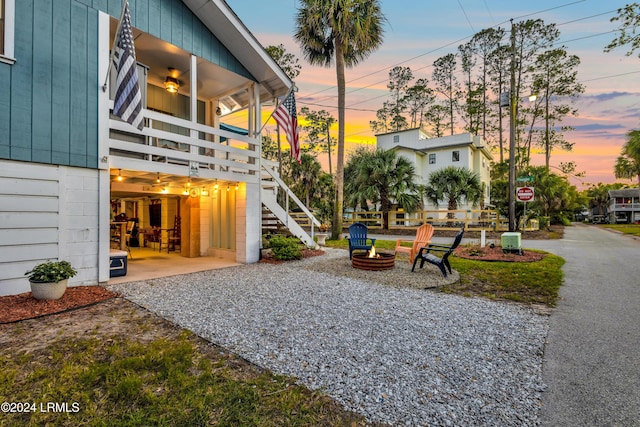 yard at dusk featuring a balcony, a patio area, ceiling fan, and a fire pit