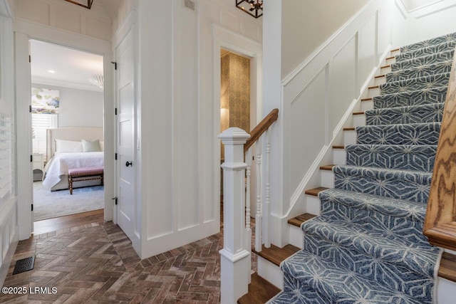 staircase featuring a decorative wall, brick floor, visible vents, and crown molding