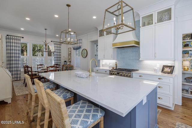 kitchen with crown molding, a center island with sink, light countertops, a sink, and light wood-type flooring