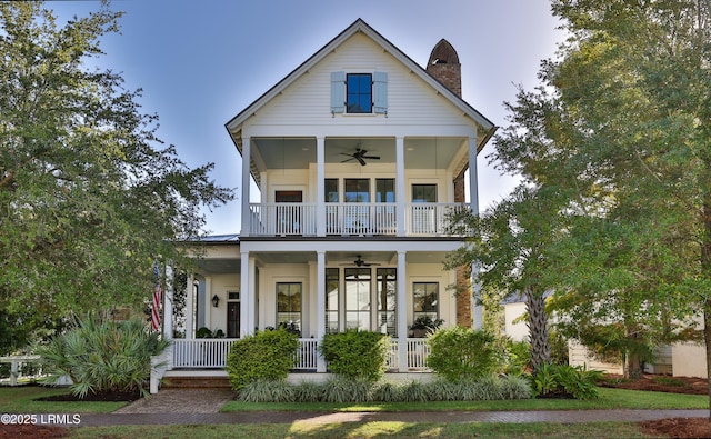 neoclassical / greek revival house featuring a chimney, covered porch, ceiling fan, and a balcony