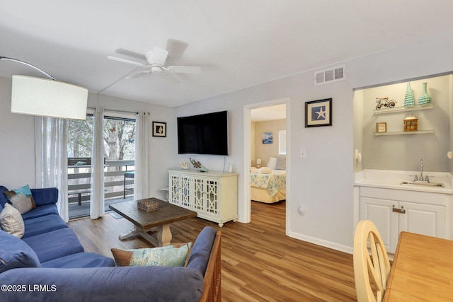 living room with ceiling fan, wet bar, and light wood-type flooring