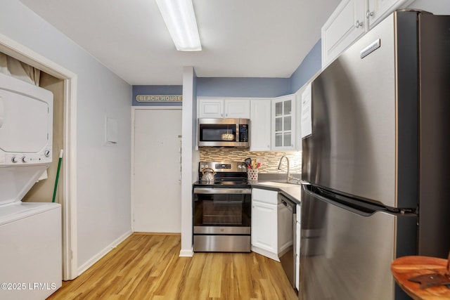 kitchen featuring stacked washer / dryer, sink, white cabinets, decorative backsplash, and stainless steel appliances