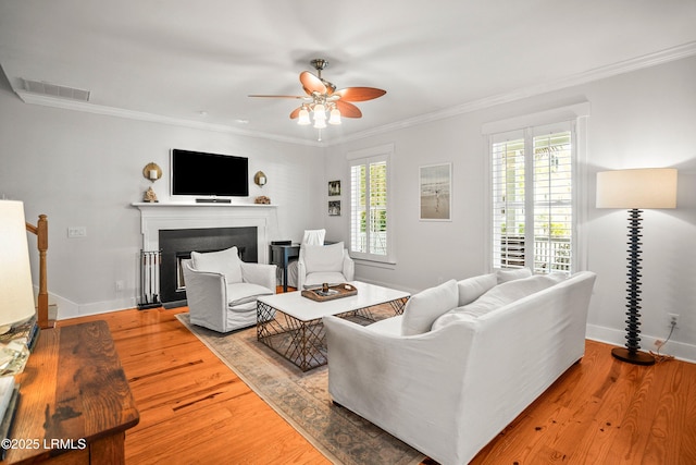living area with a ceiling fan, visible vents, crown molding, a fireplace, and wood finished floors