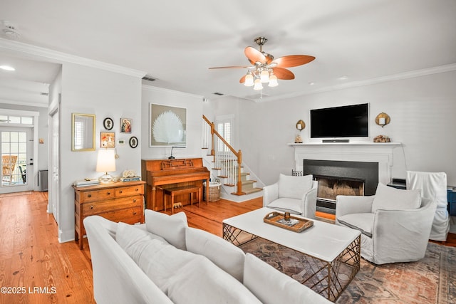 living area featuring ornamental molding, a fireplace, a ceiling fan, and light wood-type flooring
