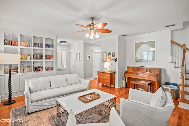 living room with visible vents, crown molding, wood finished floors, ceiling fan, and stairway