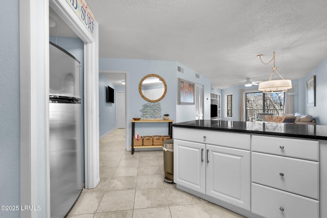 kitchen with light tile patterned floors, a textured ceiling, stainless steel fridge, and white cabinets