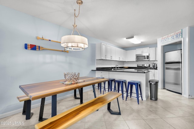 kitchen with a breakfast bar, tasteful backsplash, white cabinetry, hanging light fixtures, and stainless steel appliances