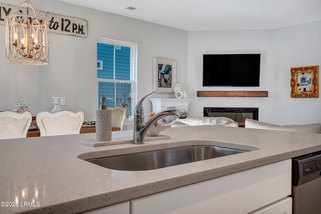 kitchen featuring a notable chandelier, light stone counters, dishwasher, a sink, and white cabinetry