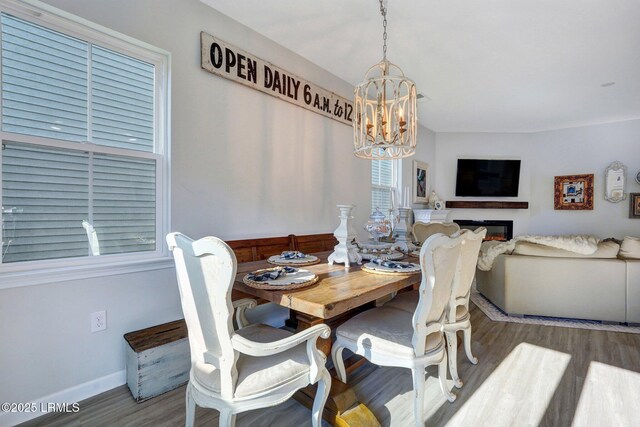 dining area with baseboards, wood finished floors, a glass covered fireplace, and a notable chandelier