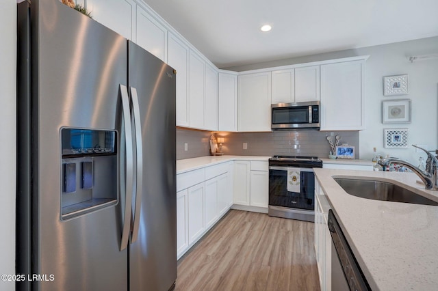 kitchen featuring stainless steel appliances, a sink, light wood-style floors, white cabinetry, and decorative backsplash