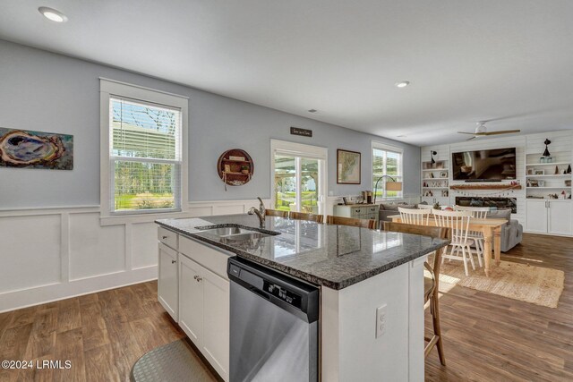 kitchen with built in features, dishwasher, white cabinetry, an island with sink, and dark stone counters