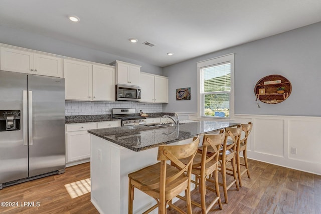 kitchen featuring white cabinetry, stainless steel appliances, a kitchen breakfast bar, and dark stone counters