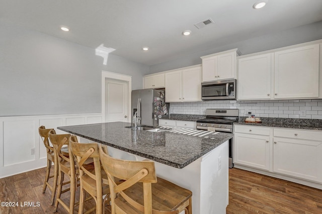 kitchen with a kitchen island with sink, white cabinetry, stainless steel appliances, and a kitchen bar