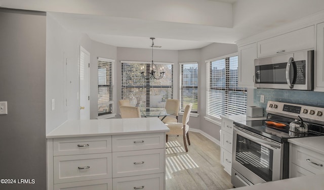 kitchen with white cabinetry, a chandelier, hanging light fixtures, stainless steel appliances, and decorative backsplash