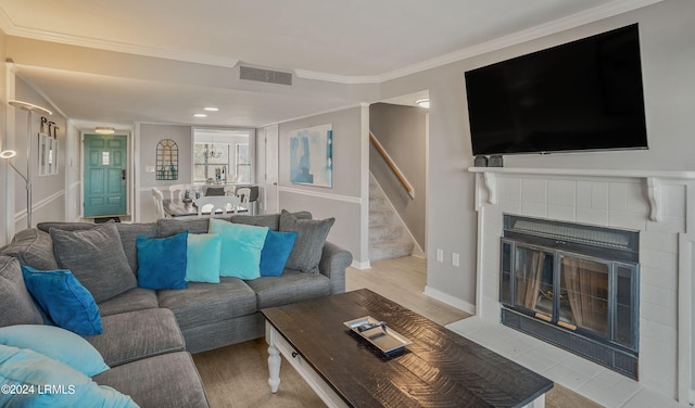 living room with a tile fireplace, ornamental molding, and light wood-type flooring