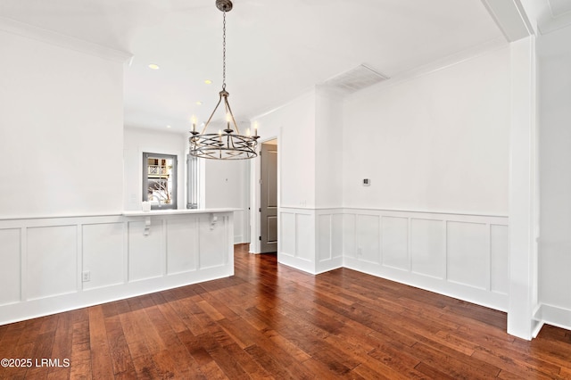 unfurnished dining area featuring visible vents, ornamental molding, dark wood-type flooring, a decorative wall, and a notable chandelier