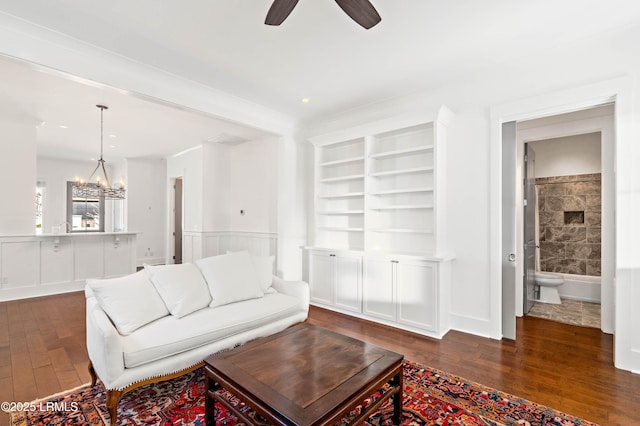 living room with hardwood / wood-style floors, built in shelves, ceiling fan with notable chandelier, and wainscoting