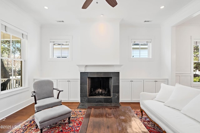 living area with a tiled fireplace, a healthy amount of sunlight, and ornamental molding