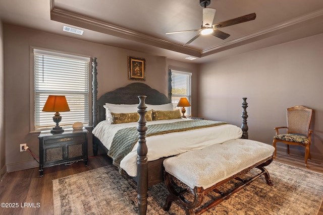 bedroom featuring visible vents, baseboards, a tray ceiling, and wood finished floors