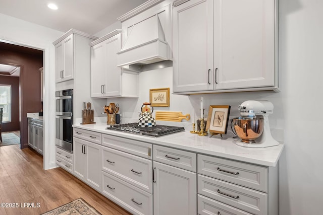 kitchen with stainless steel appliances, light stone countertops, white cabinets, custom exhaust hood, and light wood-type flooring